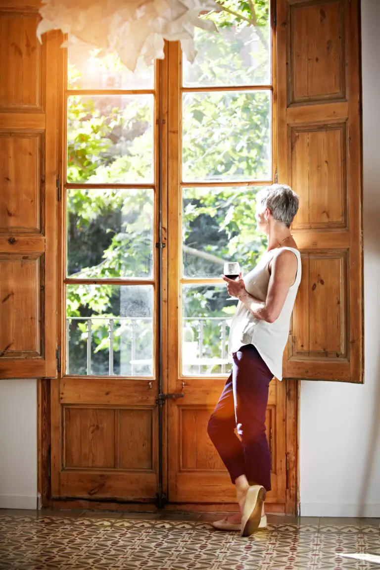 Shot of a mature woman standing by a window at home drinking a glass of wine