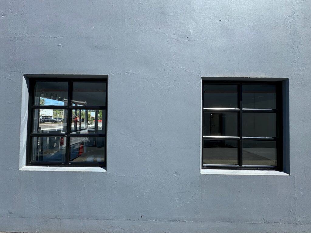 Two dark framed commercial windows in a grey exterior wall