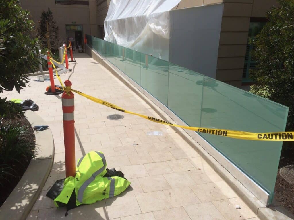 Glass balustrade panels being set along a walkway behind caution tape