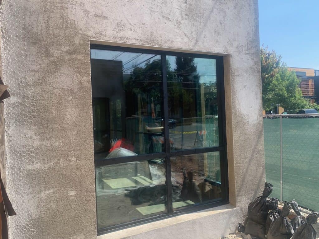 Large fixed window set into a concrete wall reflecting surrounding trees
