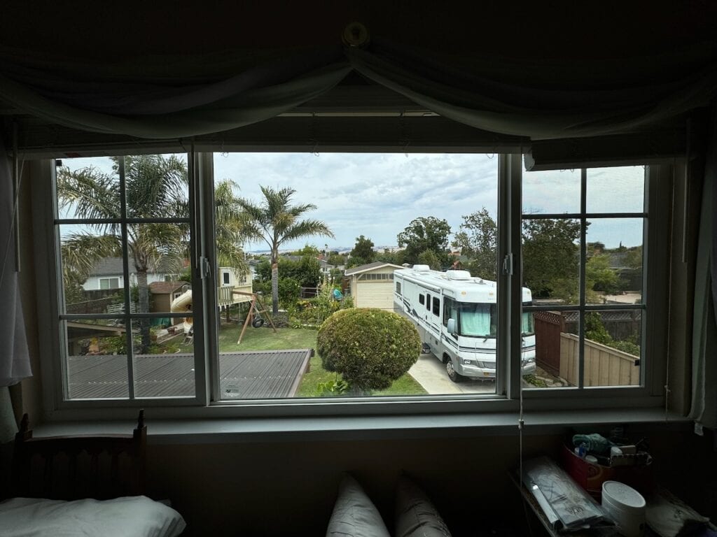 Interior view through a newly installed residential picture window overlooking a yard with a palm tree