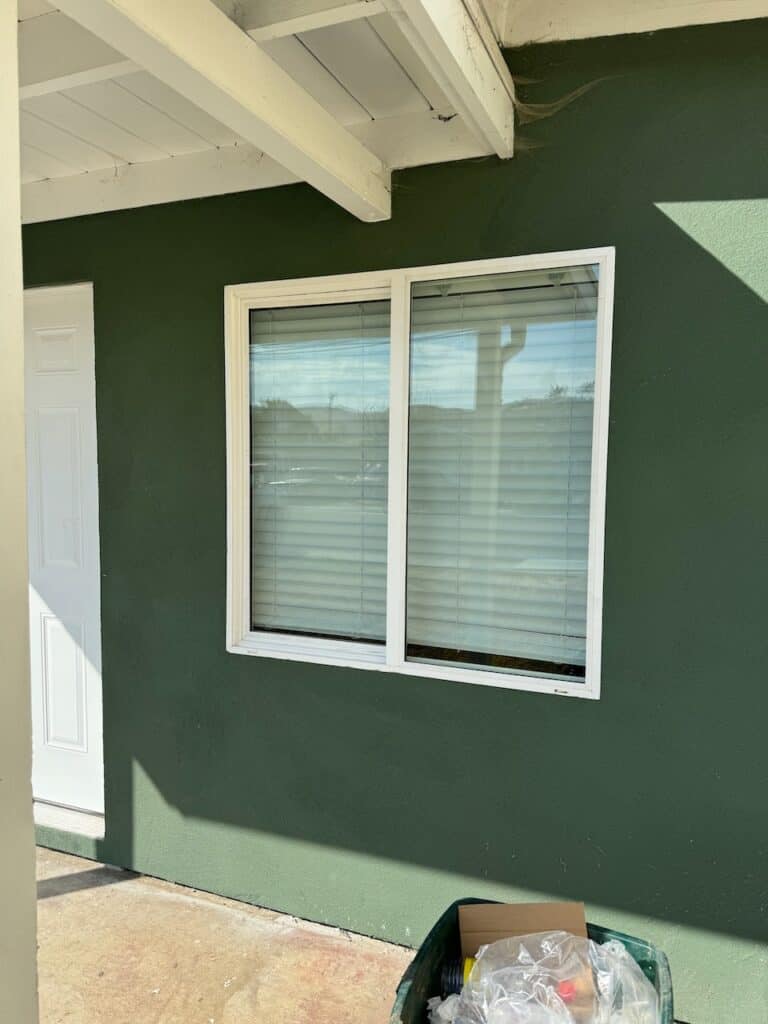 White framed sliding window installed in a green stucco exterior wall